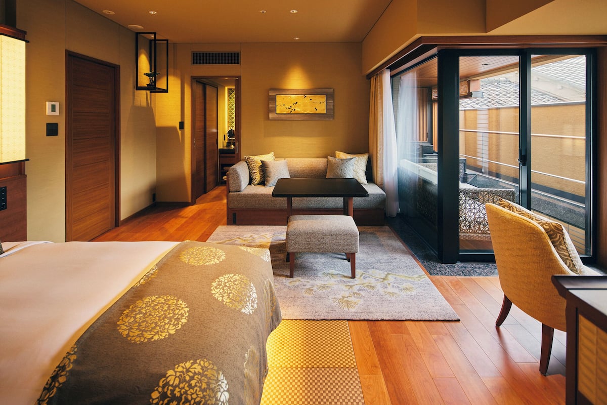 Une chambre d’hôtel avec un lit, un canapé, une petite table et une chaise. Il y a une fenêtre donnant sur l’extérieur.