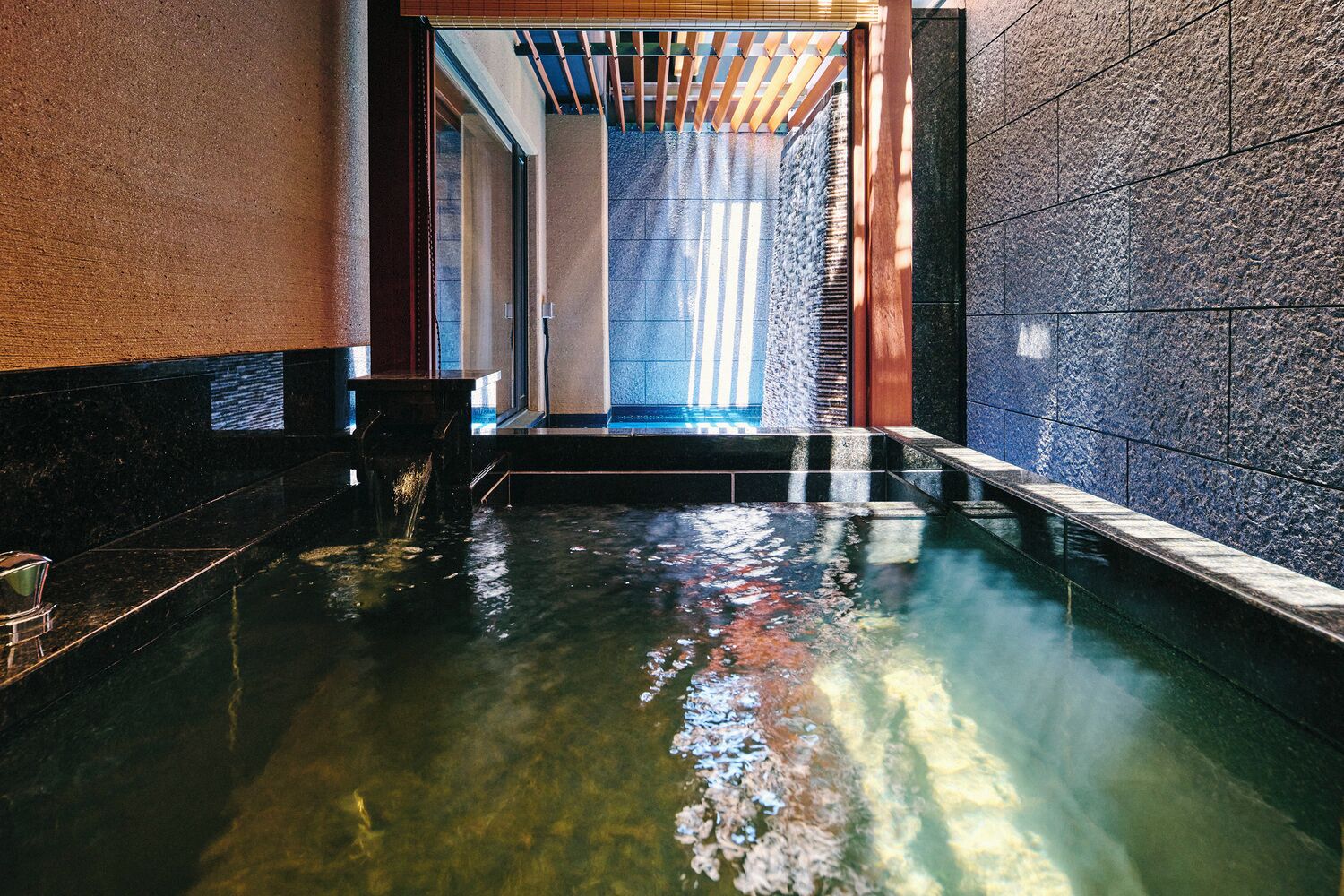 A serene indoor pool area with clear water, stone walls, and a wooden ceiling structure.
