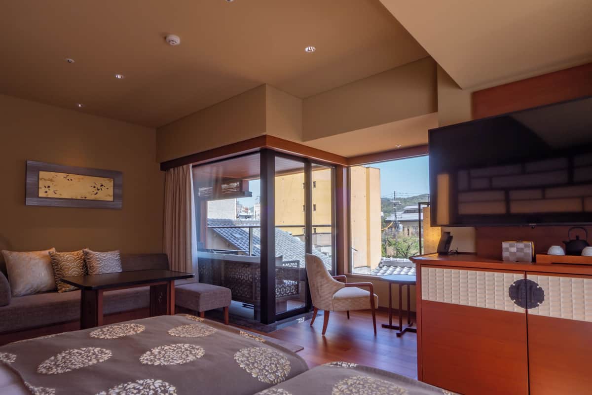 Une chambre d’hôtel avec un canapé, une petite table, une télévision et un balcon offrant une vue sur la ville.