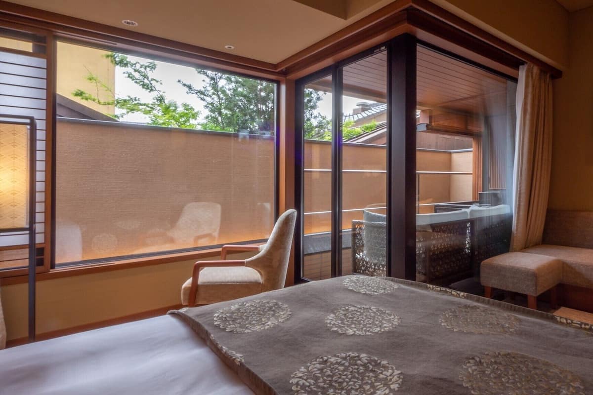 A hotel room with a bed, a seating area, and a balcony with a view of greenery.