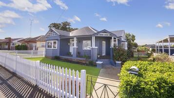 Two-story house with a gabled roof and covered porch, set amidst a well-maintained lawn and a white picket fence.