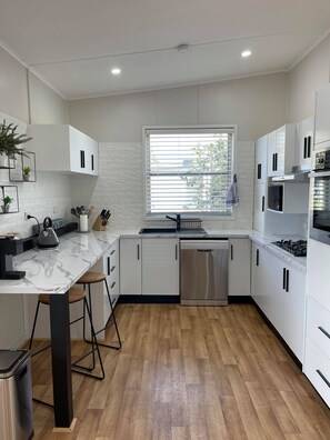 Una cocina moderna con armarios blancos, encimera de mármol, lavavajillas de acero inoxidable y suelo de madera.