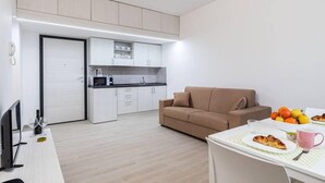 Un apartamento moderno con kitchenette, un sofá, una mesa de comedor con comida y bebidas, y un televisor.