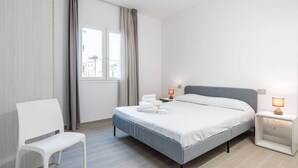 Una habitación de hotel moderna con una cama, una silla, una mesita de noche y un ventanal con cortinas.