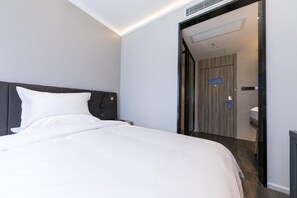 A modern hotel room with a large bed, a nightstand, a wall-mounted lamp, and a door leading to a bathroom. - Hanting Hotel (Shanghai)