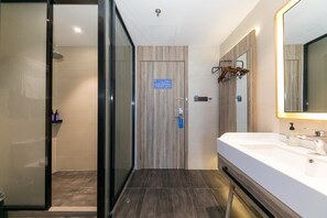 A modern bathroom with a glass shower enclosure, a wooden door with a blue sign, a large mirror, and a white sink. - Hanting Hotel (Shanghai)
