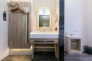 A modern bathroom with a wooden vanity, a glass shower enclosure, and a small wooden side table with toiletries. - Hanting Hotel (Shanghai)