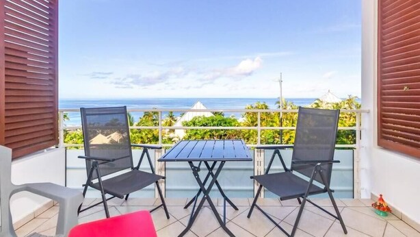 A balcony with two chairs and a table, overlooking a coastal view. - Océanides - Renovated studio with magnificent sea view (Saint-Paul)