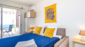 A modern bedroom with a large bed, a balcony with a view, and a colorful abstract painting on the wall. - Océanides - Renovated studio with magnificent sea view (Saint-Paul)
