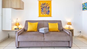 A modern living room with a grey sofa, two yellow cushions, a wall-mounted abstract painting, and a small table with a lamp. - Océanides - Renovated studio with magnificent sea view (Saint-Paul)