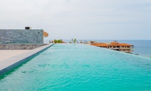 Ein Infinity-Pool mit freiem Blick auf den Ozean, einer Steinmauer und einem Gebäude mit einem Ziegeldach.