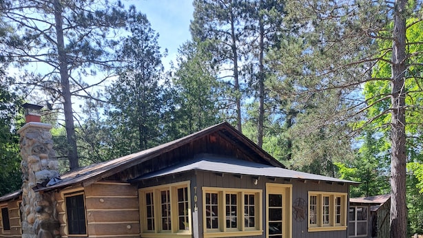 A rustic cabin with a stone chimney, multiple windows, and a well-maintained lawn.