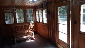 A wooden cabin interior with a bench, large windows, and a ceiling fan.