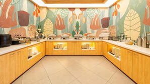 Une cuisine moderne avec des meubles en bois, un îlot central servant de buffet pour présenter les plats, et une fresque murale abstraite et colorée.