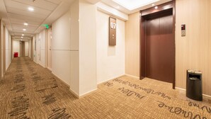 A hotel hallway with a carpeted floor, a door labeled "07", an elevator, and a trash bin. - Hanting Hotel (Dalian)