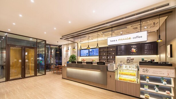 A modern coffee shop interior with a reception desk, digital menu boards, and a refrigerated display of beverages. - Hanting Hotel (Dalian)