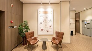 A modern waiting area with two leather chairs, a small table, a potted plant, and a wall-mounted poster. - Hanting Hotel (Dalian)