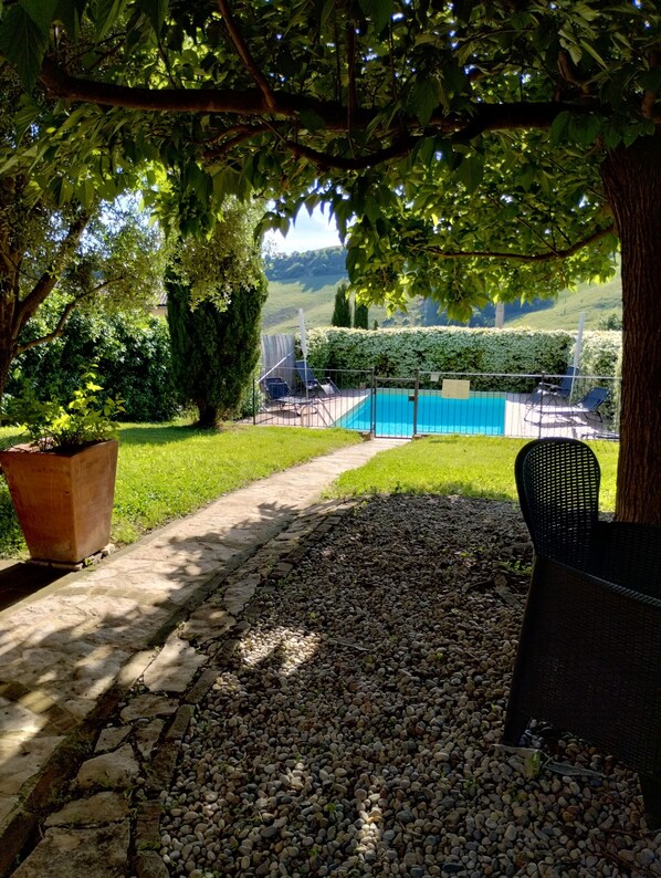 A pool area with a stone pathway leading to a pool, surrounded by greenery and a view of hills.