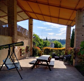 Eine Terrasse im Freien mit einem Holztisch, Stühlen, einer Schaukel und Blick auf die Landschaft.