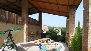 An outdoor patio with a wooden table and chairs, a green umbrella, and a wooden swing.