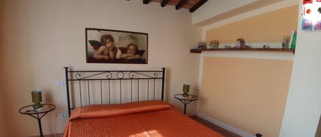 A bedroom with a bed, two nightstands, a painting, and a shelf with decorative items.