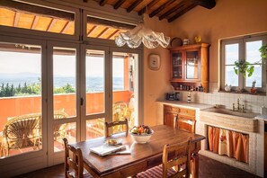 A dining area with a table set for two, a view of the outdoors, and a kitchen with wooden cabinets and a window.