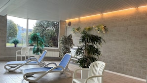 Un espace intérieur lumineux, aménagé avec des fauteuils confortables, des plantes en pot et offrant une vue sur la verdure environnante.