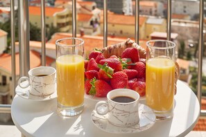 Morgenmad på en balkon med udsigt over byen, bestående af to glas appelsinjuice, en kop kaffe og en kurv jordbær.