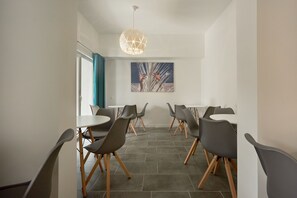 Et moderne spiseområde med runde borde og grå stole, en geometrisk pendel og et billede på væggen.