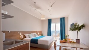A modern hotel room with a bed, a dining table with food and drinks, a small kitchen area, and a balcony with a view. - Larimar (Becici)