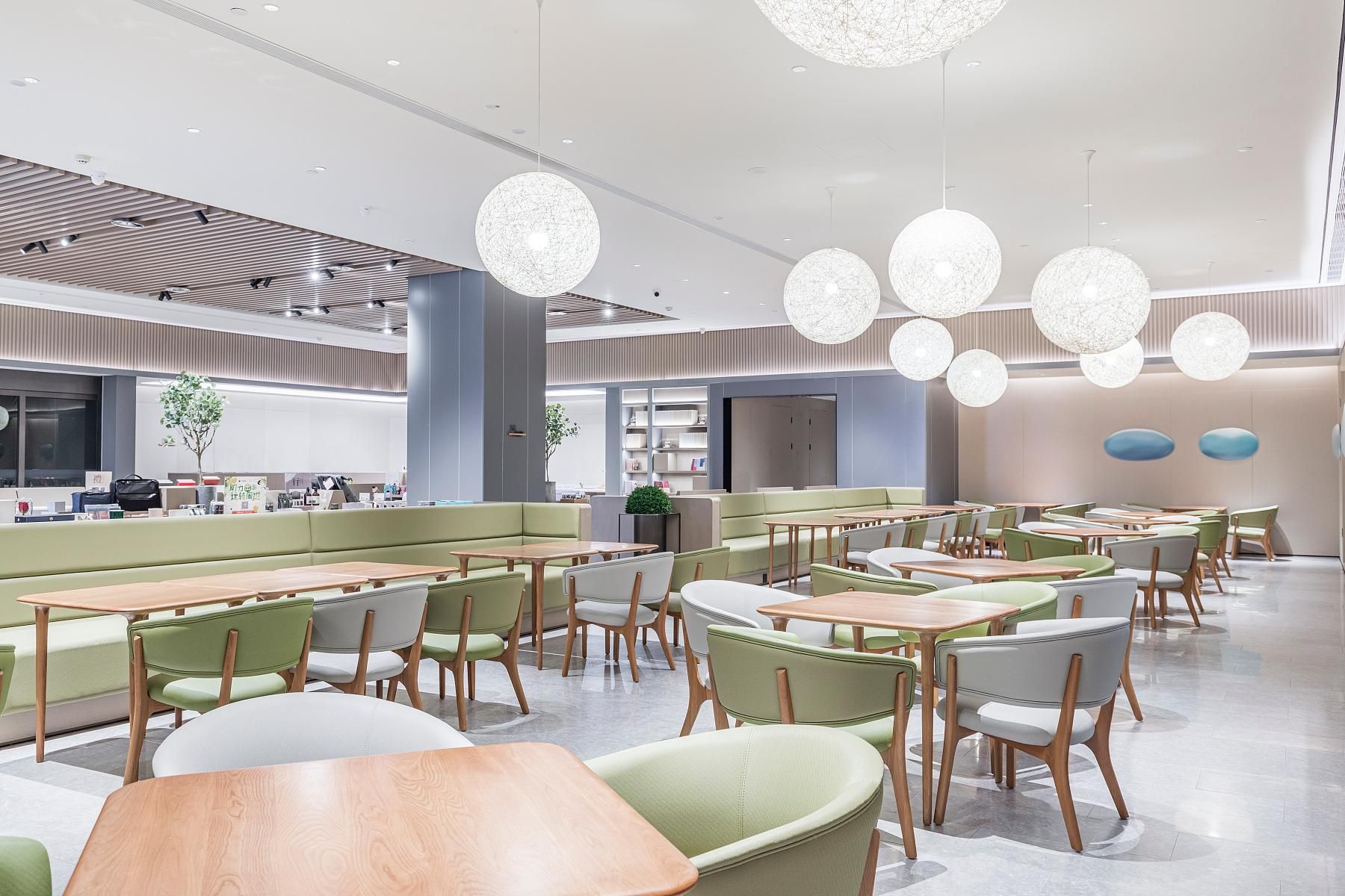 A modern dining area with round tables, green cushioned seating, and pendant lighting.