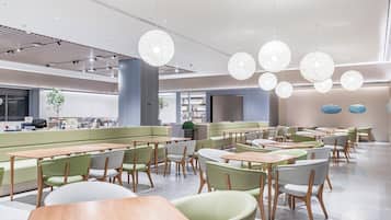 A modern dining area with round tables, green cushioned seating, and pendant lighting.