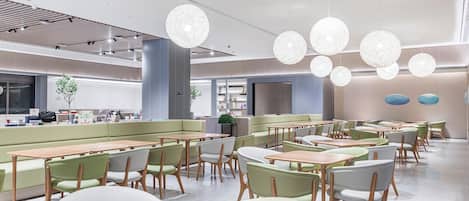 A modern dining area with round tables, green cushioned seating, and pendant lighting.