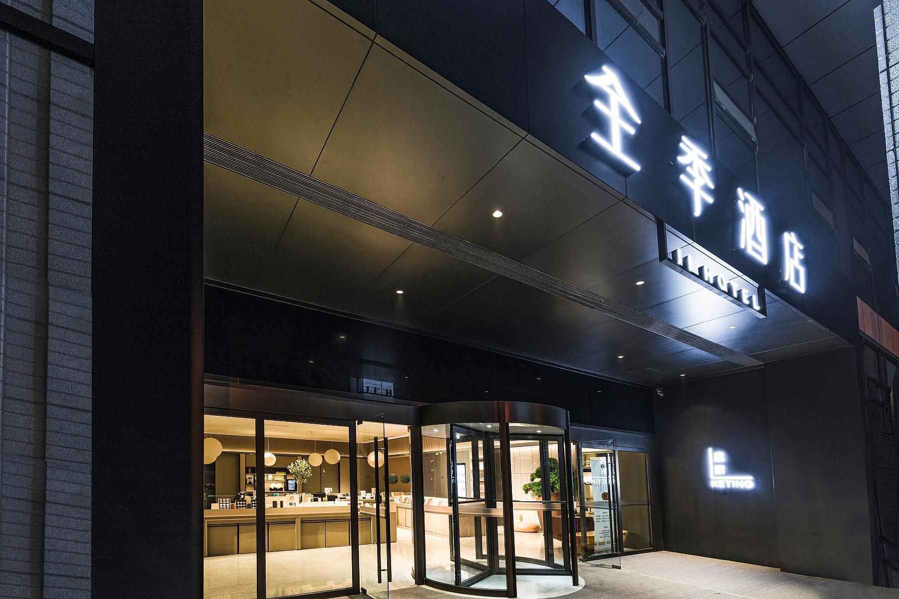 Entrada de hotel com porta giratória, balcão de recepção e letreiro com caracteres chineses.