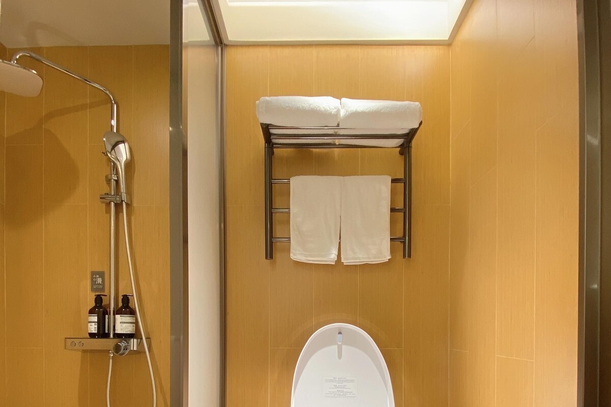 A modern bathroom with a glass-enclosed shower, a toilet with a towel rack above, and a trash bin.