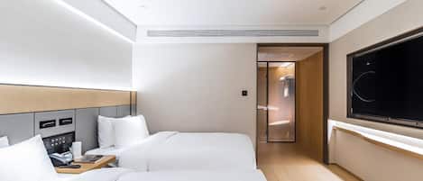A hotel room with two beds, a TV, a desk with a phone, and a shower area.