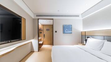 Una habitación de hotel moderna con una cama grande, televisión, zona de ducha y un cuadro en la pared.