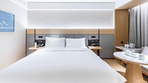 A modern hotel room with a large bed, bedside tables, a desk, and a view of the city. - JI Hotel (Nanjing)