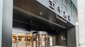 A hotel entrance with a revolving door, large glass windows, and a sign indicating the hotel name.