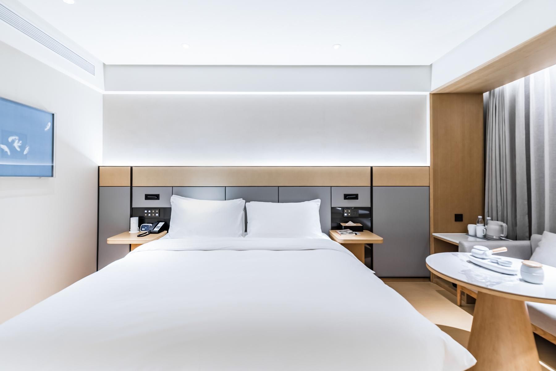 A modern hotel room with a large bed, bedside tables, a desk, and a view of the city.