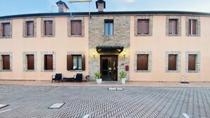 Un hotel con fachada de piedra, múltiples ventanas y un área de entrada empavedada.