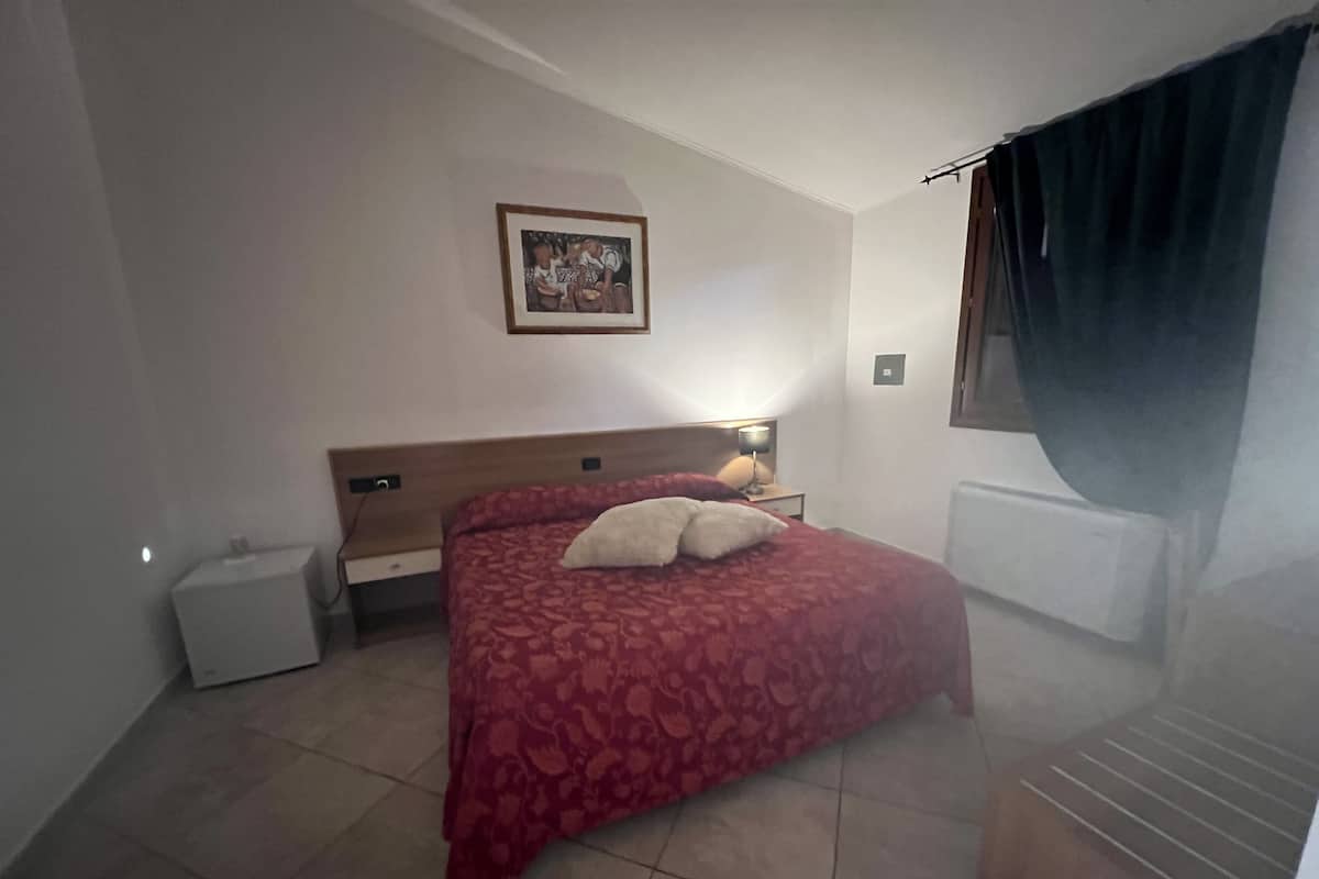 Une chambre à coucher avec un lit, une table de chevet, une lampe, un tableau au mur et une fenêtre avec des rideaux.