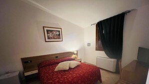 Un dormitorio con cama, mesita de noche, lámpara, radiador y ventana con cortinas.