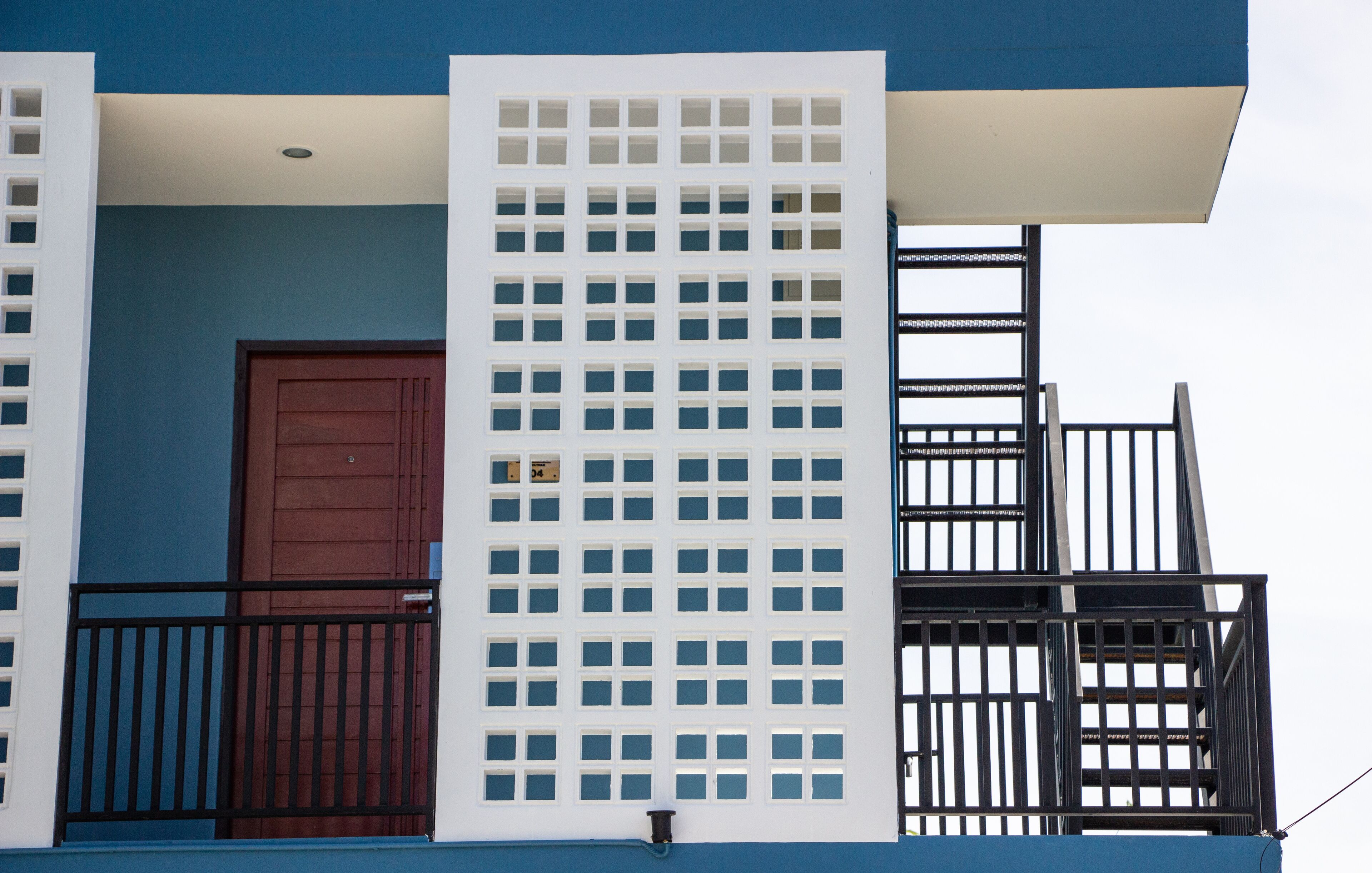 Ein Gebäude mit blauer Fassade, einer braunen Tür und einem weißen Gitterwerk.