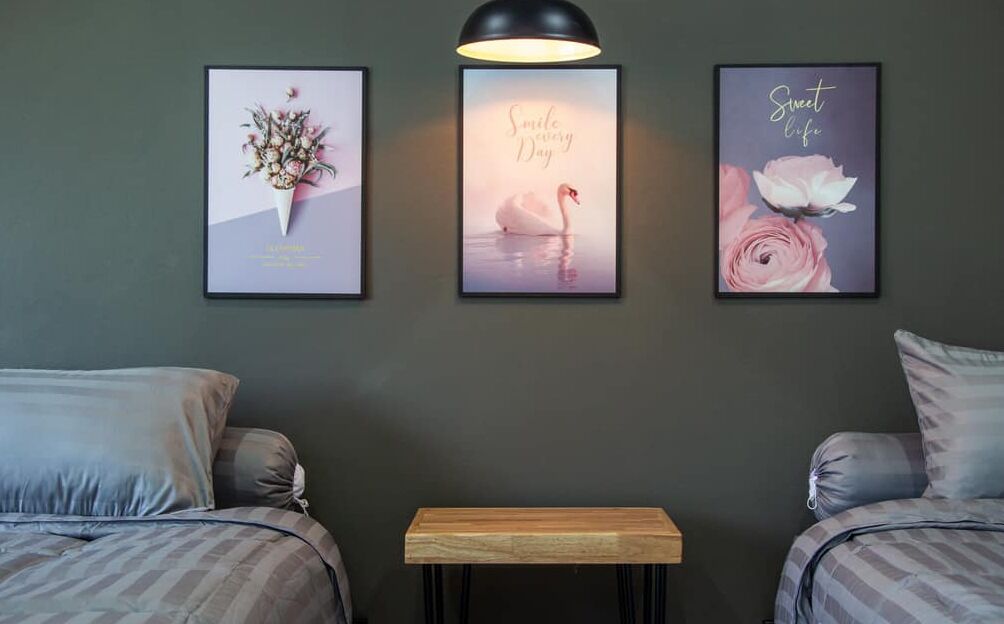 Une chambre d’hôtel avec deux lits, une petite table en bois et trois tableaux encadrés accrochés au mur.