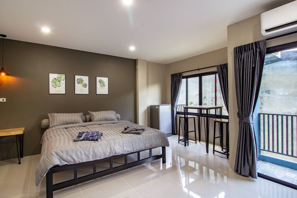 A modern bedroom with a bed, bedside tables, a small desk, and a balcony with a table and chairs.