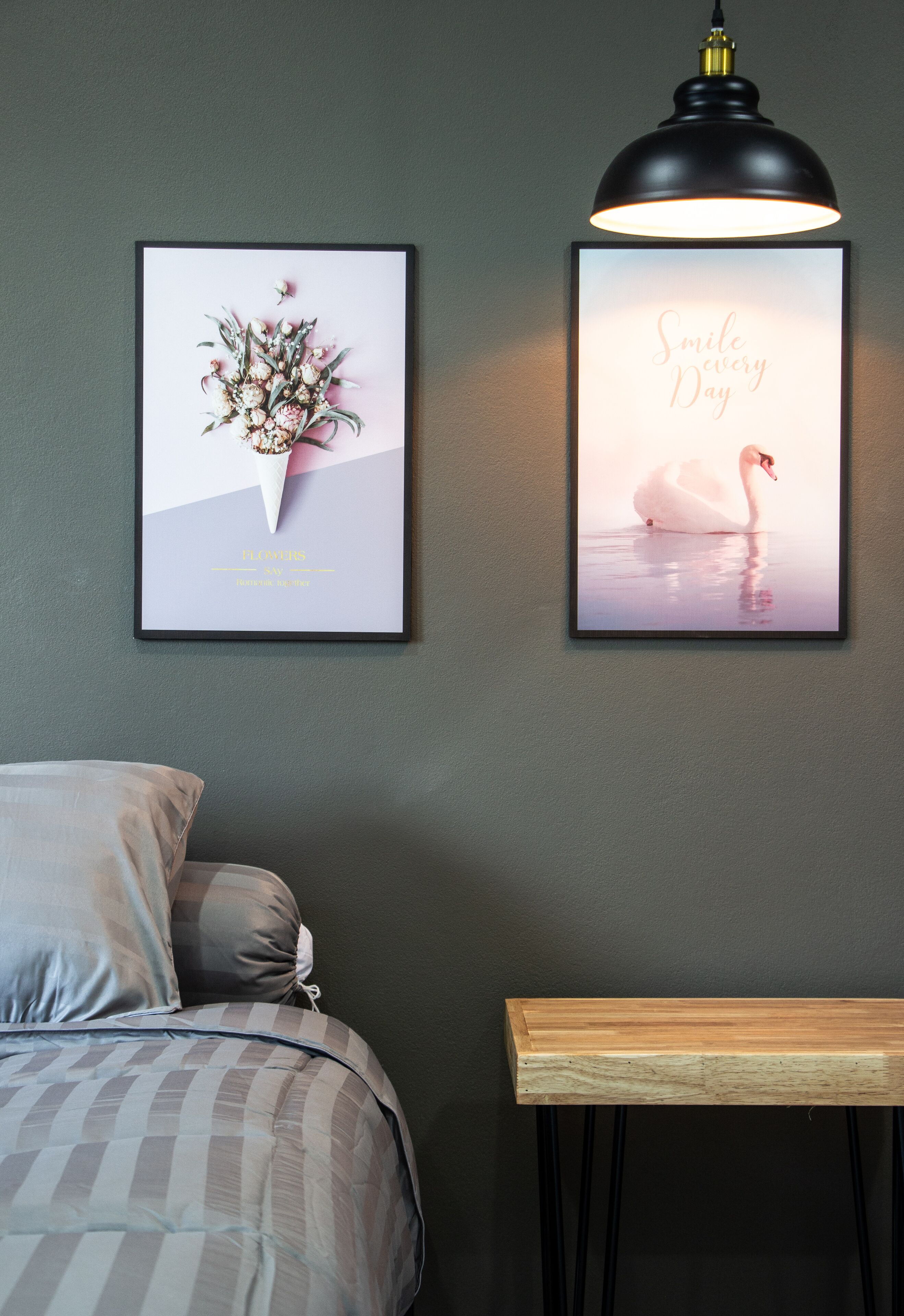 A bedroom with a bed, a framed floral artwork, a framed swan artwork, and a wall-mounted lamp.