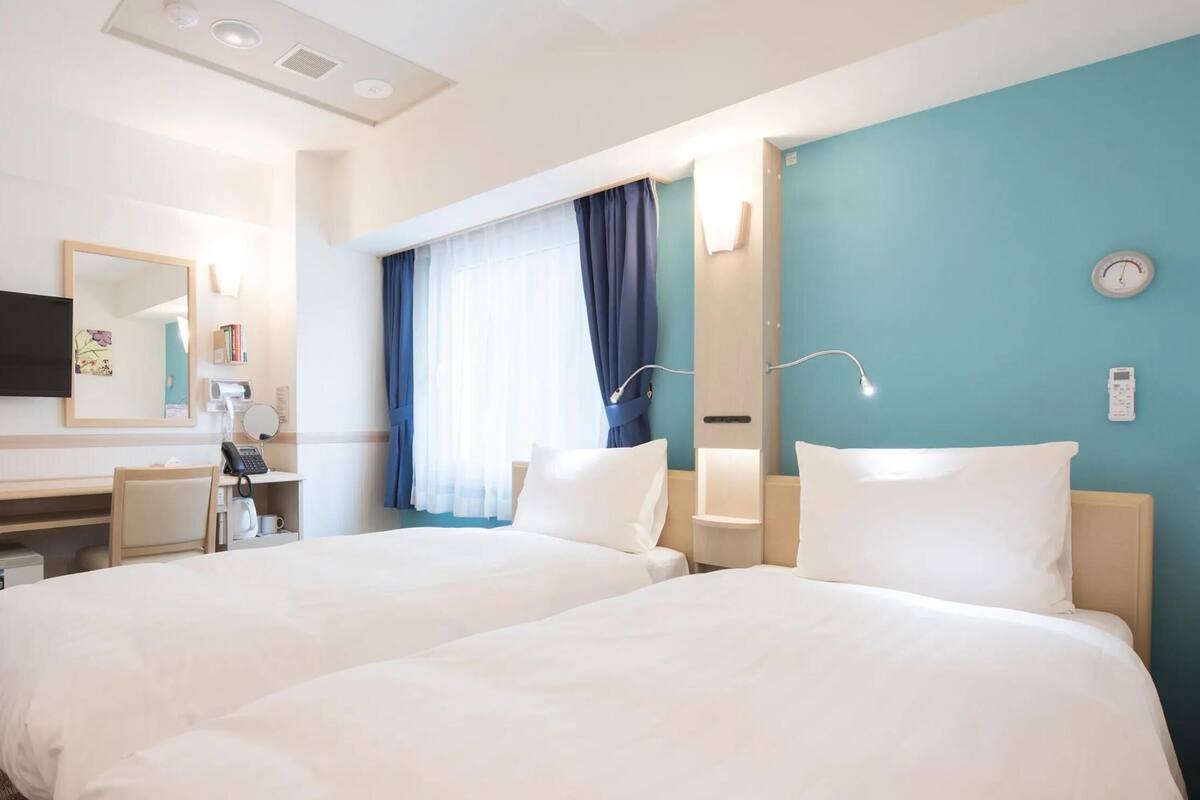 Habitación de hotel con dos camas, un escritorio con teléfono, un espejo y una ventana con cortinas.