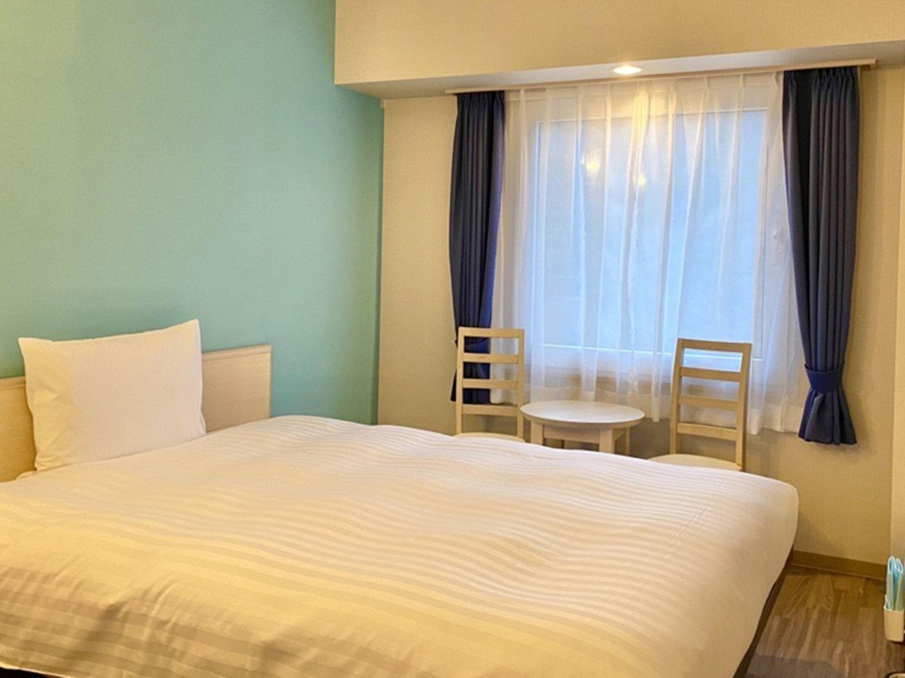 A hotel room with a large bed, two chairs, a small table, and a window with curtains.
