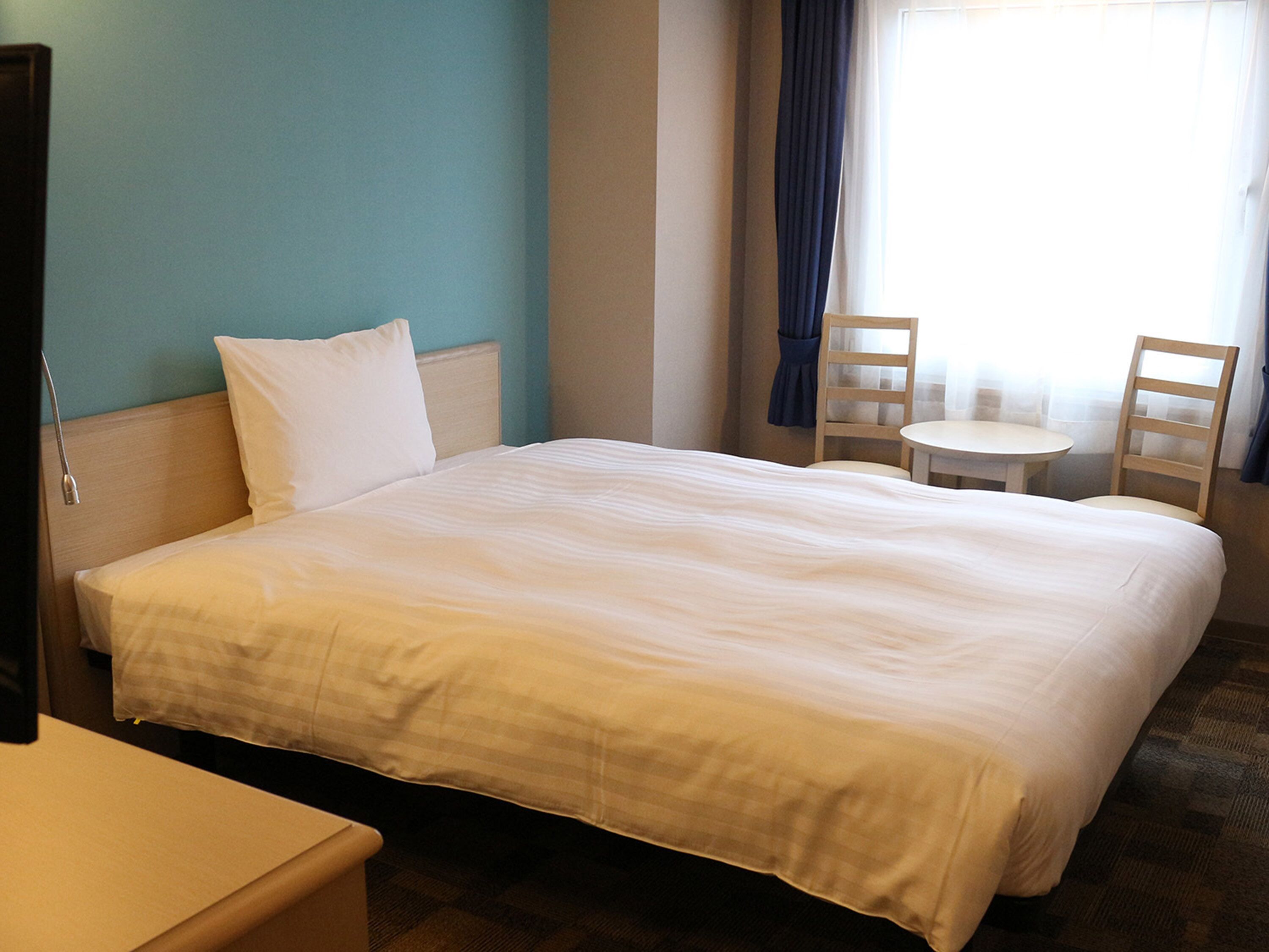A hotel room with a large bed, a small table, two chairs, and a window with curtains.